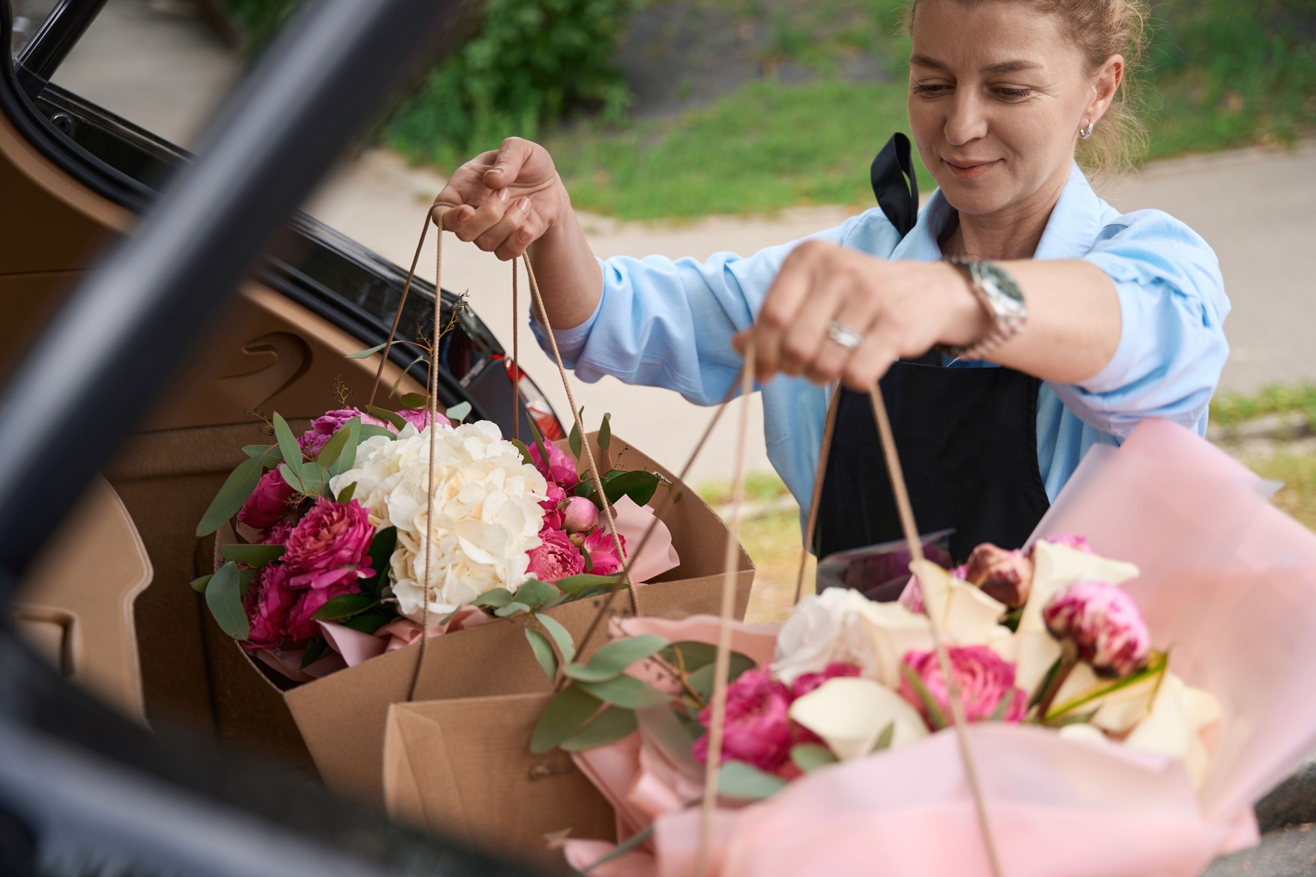 Florist puts packages with bouquets of flowers in car trunk